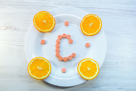 Vitamin C concept. Orange slices and citrus fruits shape pills on a white plate.の写真素材