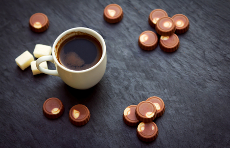 Cup of freshly brewed coffee, milk chocolate candies and sugar on black stone tray. Sweet breakfast or snack.の写真素材