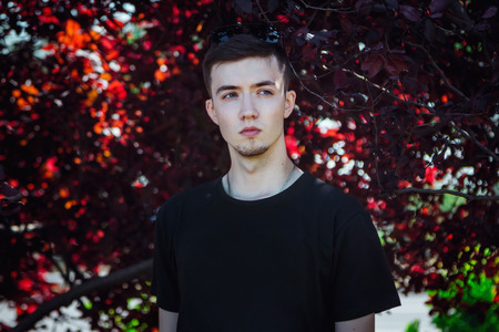 Portrait of serious handsome young man standing near the tree with red leavesの写真素材
