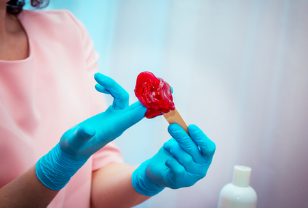 Close-up hands in red gloves preparing red berry flavor, hair removal beauty procedure.の写真素材