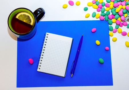 Blank spiral notepad, pen, cup of tea with lemon slice and colorful candies on the table.の写真素材