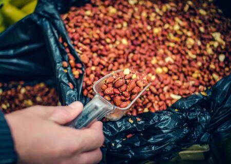 Man`s hand taking peanuts from container into a scoop at market. Selective focus.