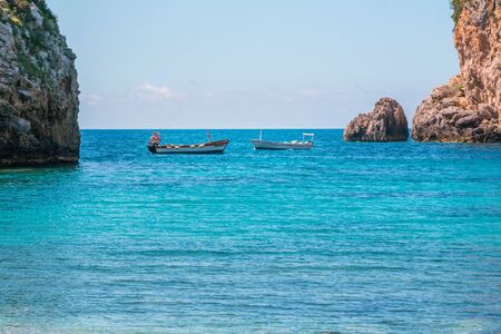 Seascape - lagoon with turquoise water, mountain with cliffs, green trees, blooming bushes, rocks in...