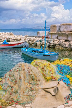 Beautiful landscape with old small fisher boat, colorful fishing nets, calm sea water, blue sky with clouds and mountains on the horizon. Corfu Island, Greece.の写真素材