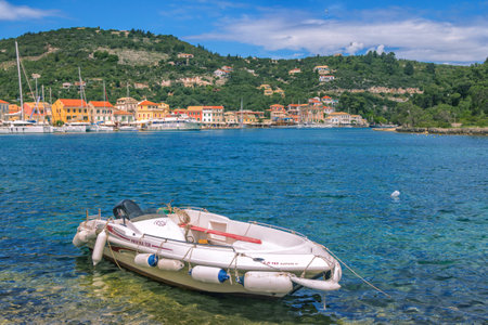 Paxos Island/Greece- May 7, 2019: view of beautiful Loggos Harbor - sea lagoon with calm turquoise water, white moored motor boat, colorful old houses and blue sky with white clouds. Summer cityscape.のeditorial素材