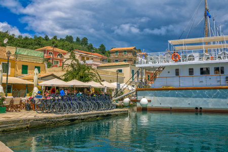 Paxos Island / Greece- May 7, 2019: view of beautiful Loggos Harbor - large white cruise ship, bicycle rent, colorful old houses and blue sky with clouds. Summer cityscape.のeditorial素材