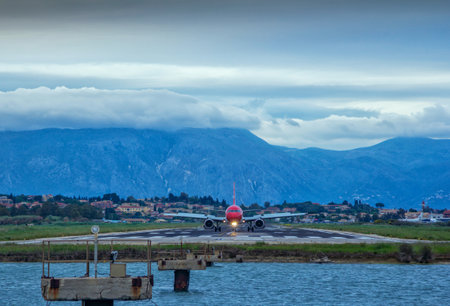 Corfu Island / Greece- May 4, 2019: view of Edelweiss airplane on runway of Corfu airport, sea, village and mountains on the horizon, green trees and clouds on the sky.のeditorial素材