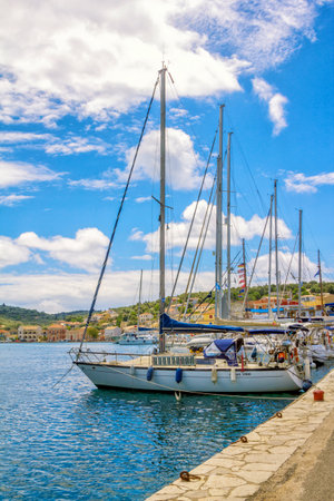 Paxos Island / Greece- May 7, 2019: view of beautiful Loggos Harbor - sea bay with calm turquoise water, ships and yachts colorful old houses and blue sky with white clouds. Summer cityscape.のeditorial素材