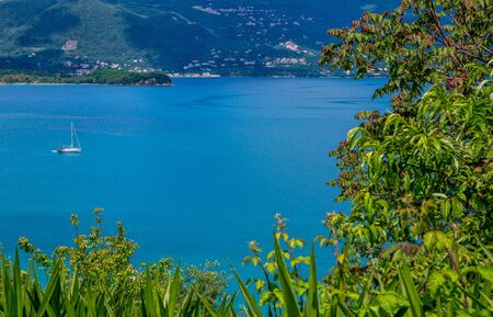 Beautiful summer landscape - calm sea water surface, white yacht, green trees and mountains on the horizon. Corfu Island, Greece.の写真素材