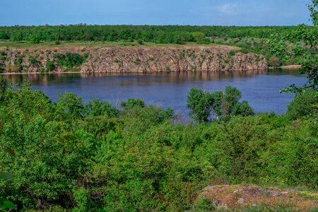 Beautiful landscape with calm river, cliffs, green lush foliage and blue sky. Spring nature.の写真素材