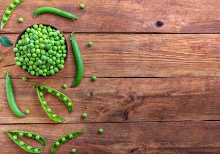 Fresh green peas in a bowl and pods on a rustic wooden tableの写真素材