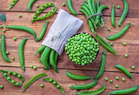 Fresh green peas in a bowl and pods on a rustic wooden table