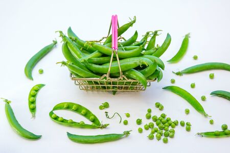 Close up fresh green peas in mini shopping store basket and pods on a white backgroundの写真素材
