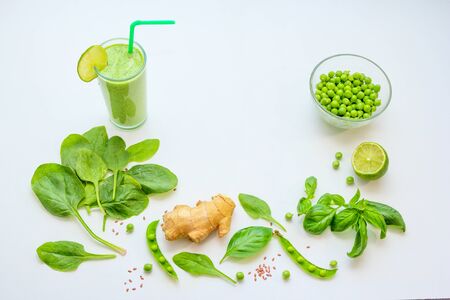 Smoothie in a glass and ingredients - green peas, ginger, basil and spinach leaves on a white background. Healthy vegan cocktail.の写真素材