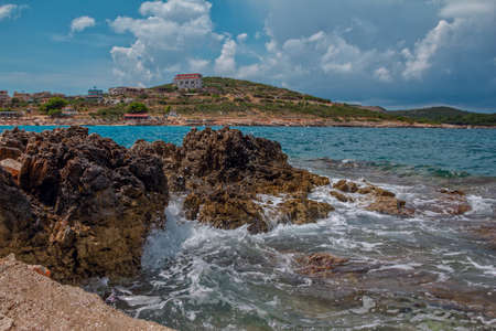 Summer landscape with stormy sea, rocks and cliffs, hills and small village on the horizon, clouds on blue sky. Albanian resortの写真素材