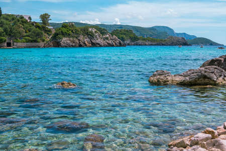 Beautiful landscape - sea lagoon with turquoise calm water, stones and rocks on the beach, blue sky. Corfu Island, Greece.の写真素材