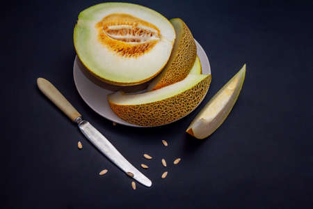 Fresh ripe juicy melon slices on a plate, knife and seeds on black tableの写真素材