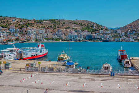 Saranda / Albania - August 5, 2020: city harbor - sea bay with calm turquoise water, ships and ferryboats, cityscape - modern buildings and hotels on the hill.のeditorial素材