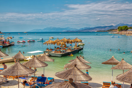 Ksamil / Albania - August 5, 2020: view of beautiful summer resort - sea bay with turquoise water, white sand, people, relaxing, tanning and swimming, blue sky and mountains on the horizonのeditorial素材