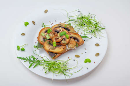 Sandwich with fried mushrooms, basil, pumpkin seeds and microgreens - radish and onion sprouts, served on white plateの写真素材