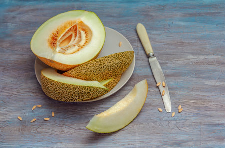 Fresh ripe juicy melon slices on a plate, knife and seeds on wooden tableの写真素材