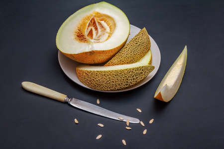 Fresh ripe juicy melon slices on a plate, knife and seeds on black tableの写真素材