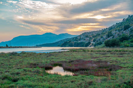 Beautiful summer landscape with lake and mountains at sunset. Green grass and clouds on the sky.の写真素材