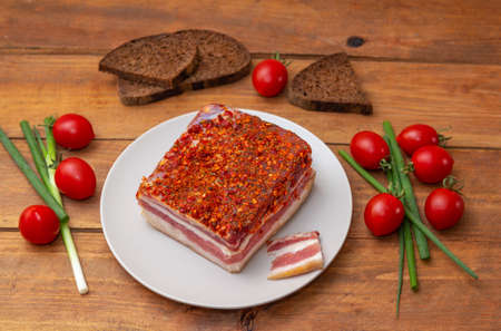 Smoked spicy bacon on a plate. Slice of smoked pork meat on bread, cherry tomatoes and green onion on wooden table.の写真素材