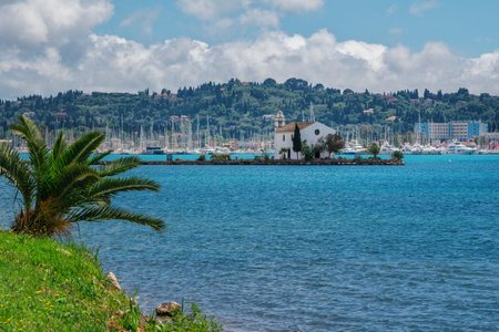 Corfu Island, Greece- May 5, 2019: View of beautiful Gouvia  marina, ancient Ypapanti church - small white house on a pier, resort village and mountains on the horizon. Summer landscape.のeditorial素材