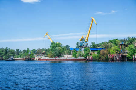 Cranes loading sand on a barge at quarry on a river coast. Sand mining â€“ industrial landscape
