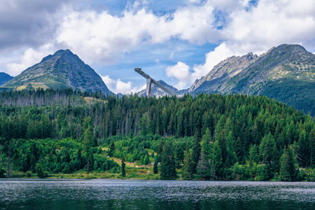 Beautiful summer landscape - mountains, lush forest, ski jumping tower and white clouds on blue sky