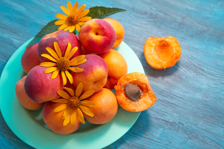 Ripe apricots decorated with yellow flowers on a plate on a wooden tableの写真素材