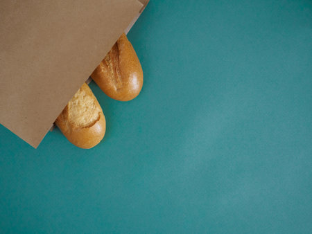 Fresh traditional french baguettes peek out of a craft brown bag on a green background. Top view, flat lay with space for text, recipe. Use for advertising a bakeryの写真素材