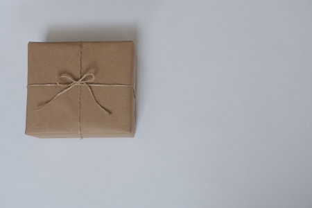 Christmas gift on a white background with place for text. The gift is packed in craft paper and tied with a canvas rope. An exquisite gift. New year, birthdayの写真素材