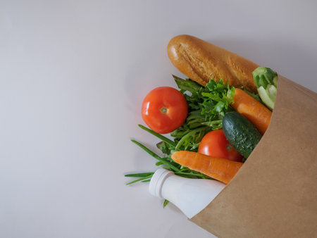Daily grocery shopping basket on a white background. Green onions, lettuce, cucumbers, tomatoes, zucchini, carrots, milk, French baguette in a craft bag. Flat lay of vegetables, herbs, bread and milk on white background with copy space, top view. Healthy food conceptの写真素材