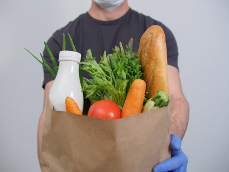 Delivery service courier holds a package of groceries close-up on a white background.の写真素材