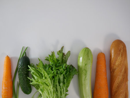 Set of food from fresh vegetables, baguette and greens on a white background, top view. Vegetarian food, healthy food, vitamins. Flat lay of carrots, zucchini, cucumber, baguette, lettuceの写真素材