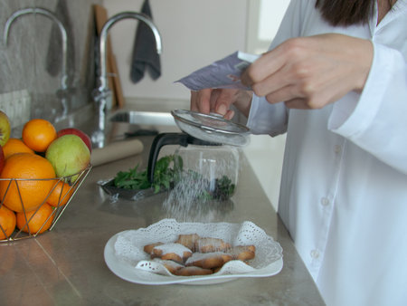 Female hands sprinkle homemade cookies with powdered sugar through a sieve on the background of the...