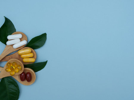 Flat lay of vitamins, minerals, pills in wooden spoons and green leaves on a light blue backgroundの写真素材
