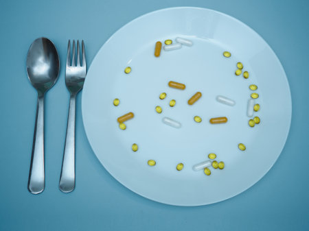 White plate on a blue background full of vitamins and minerals in the form of multi-colored capsules. Supports health and immunity. Care and health concept. Taking vitaminsの写真素材