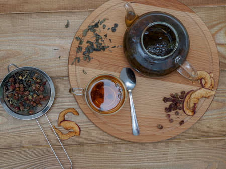 Tea composition on a wooden background top view. A cup of freshly brewed aromatic black tea with mint, chamomile and dried strawberries on a wooden tray. Natural organic delicious tea in a transparent glass cup. Flat layの写真素材