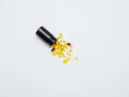 Many different vitamins and medical pills are poured from a dark plastic jar on a white background. Vitamin D, B, omega 3, zinc calcium to support immunityの写真素材