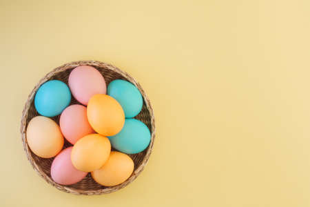 Many Easter colored eggs in pastel colors in a wicker basket on a yellow background with copy space, top view, flat layoutの写真素材
