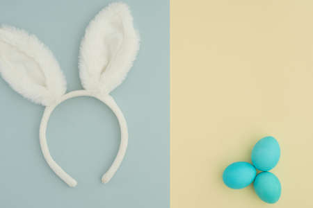 A minimalistic two-tone background in pastel shades cut in half. Easter background with bunny white ears on a blue background and three blue Easter eggs on a yellow background. Space for text. Creative easter backgroundの写真素材