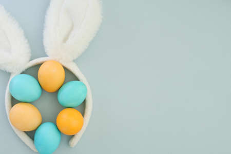Creative minimalistic composition with bunny ears and colorful Easter eggs in pastel shades of blue and yellow. Space for text, flat lay, top view, soft blue backgroundの写真素材