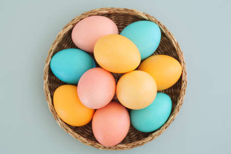 A full basket of colorful Easter eggs in pastel colors on a soft blue background. Easter concept. Minimalistic Easter composition. Flat lay, top view.の写真素材