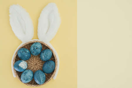 Creative Easter composition with stylishly painted blue eggs in a basket and white bunny ears on a...