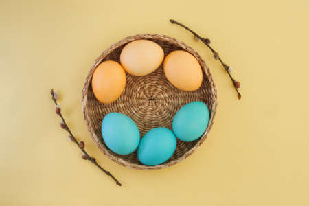 Easter eggs painted in gentle pastel colors of yellow and blue in a wicker basket and pussy willow branches on a trendy yellow background. Easter background. Top view, flat layの写真素材