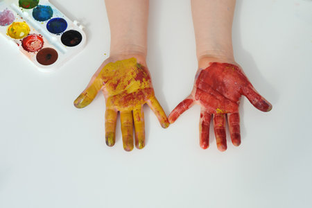 Multi-colored palms of a child after drawing lessons. Drawing with the palm of your hand. Creative development of the child. Childs hands in red and yellow watercolor paint. View from aboveの写真素材