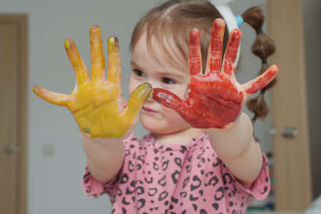 A funny girl painted her palms with watercolors in red and yellow and shows them to the camera. The...